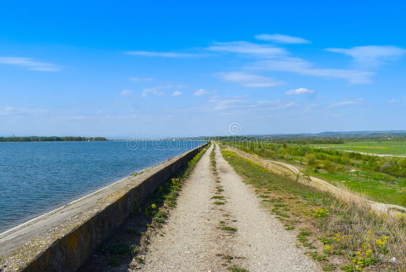 Landstra?e entlang der Seeverdammung an einem sonnigen Sommertag mit perfektem blauem Himmel stockbild Landstra?e entlang der Seeverdammung an einem sonnigen Sommertag mit perfektem blauem Himmel stockbild