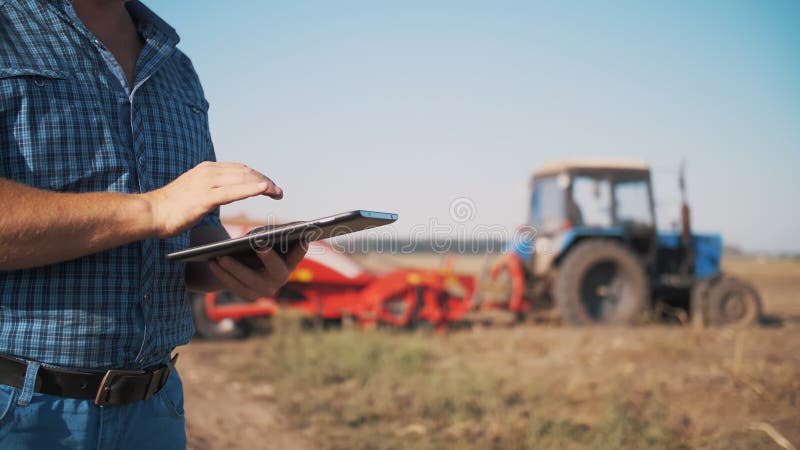 Landwirt nutzt digitale Tablette. schließen. auf dem landwirtschaftlichen Feld in der Nähe von Zugmaschinen. intelligente Landwirt