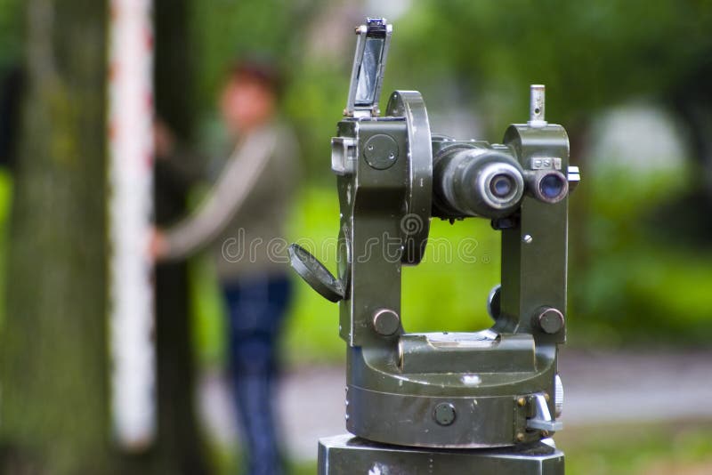 Land survey instrument called a Theodolite with man in the background holding a vertical measuring rod. Land survey instrument called a Theodolite with man in the background holding a vertical measuring rod.