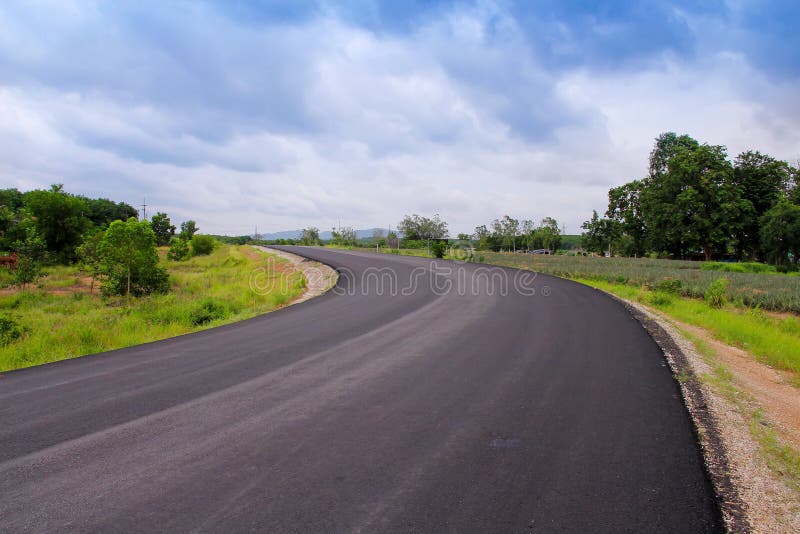 Lange leere Asphaltstraße mit buntem grünem Baum, Gras auf der Seite auf Hintergrund des blauen Himmels und weißes bewölktes stockbild Lange leere Asphaltstraße mit buntem grünem Baum, Gras auf der Seite auf Hintergrund des blauen Himmels und weißes bewölktes stockbild