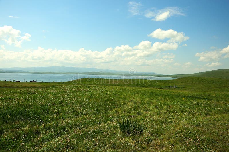 Lange Veld und einige kleine Häuser auf der Seite eines Hügels an der Küste von einem großen malerischen See stockfoto