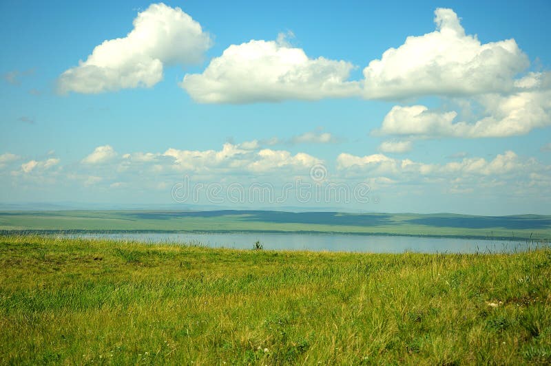 Lange Veld und einige kleine Häuser auf der Seite eines Hügels an der Küste von einem großen malerischen See stockfotos