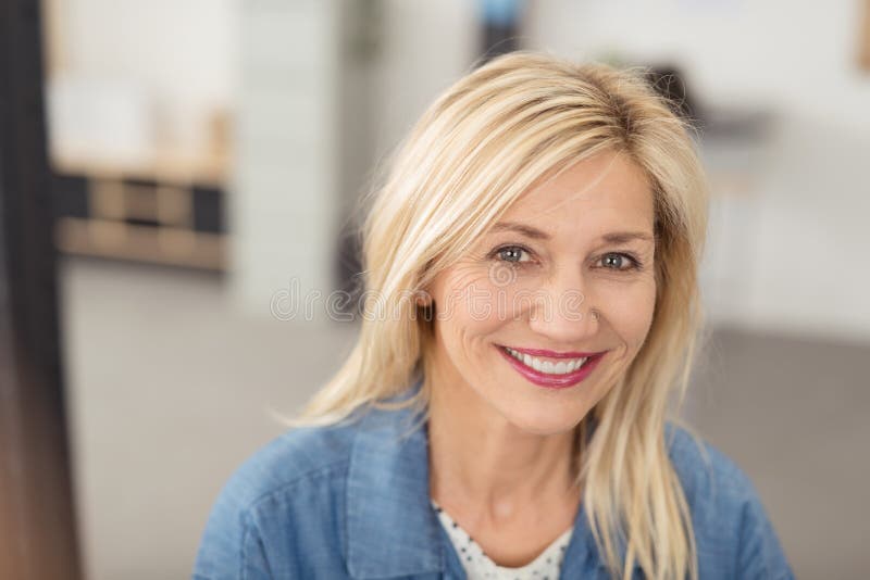 Long-haired blond woman with a joyful facial expression smiling at camera with blue eyes and white teeth, portrait indoors. Long-haired blond woman with a joyful facial expression smiling at camera with blue eyes and white teeth, portrait indoors