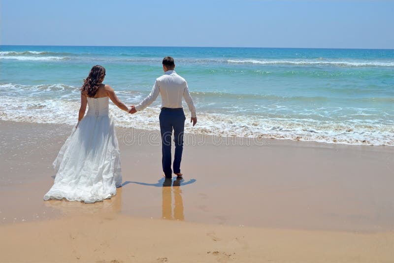 Langhaarige Brunettebraut und -bräutigam in einer Klage Jungvermähltenhändchenhalten, geht zum Sand im Wasser des Indischen Ozean stockbilder Langhaarige Brunettebraut und -bräutigam in einer Klage Jungvermähltenhändchenhalten, geht zum Sand im Wasser des Indischen Ozean stockbilder