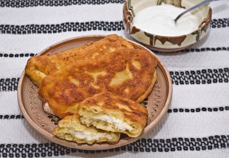 Langos (fried dough - doughnuts) filled with salte. D cheese. All setup in Romanian traditional earthenware on a rustic towel. Alongside a pot with sour cream stock images Langos (fried dough - doughnuts) filled with salte. D cheese. All setup in Romanian traditional earthenware on a rustic towel. Alongside a pot with sour cream stock images