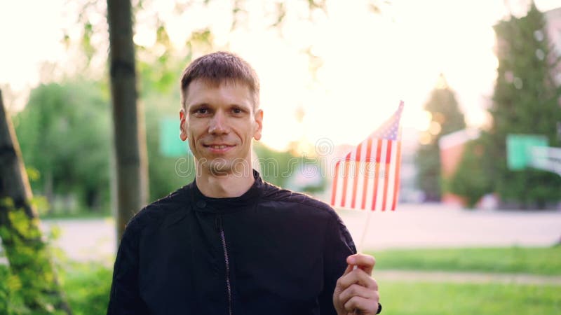 Langzaam motieportret van de Amerikaanse mens die nationale vlag van de V.S. golven, en camera glimlachen bekijken Gelukkige jong