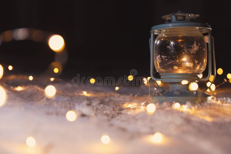 Lantern with Burning Candle and Christmas Lights on Snow Outdoors