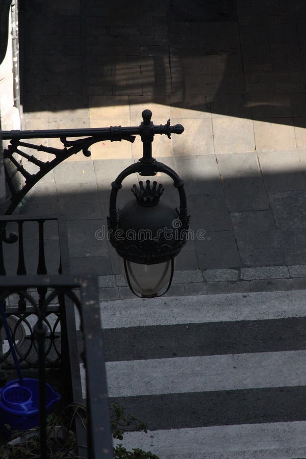 Lantern and shadows creating a graphic composition. Urban photography, light interplay, and a sense of place. Close-up of a lantern, showcasing its design and the dramatic shadows it casts. Urban detail, light, and form.