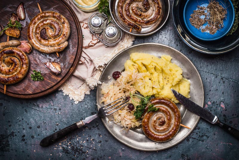 Lantlig mat med den grillade korven mosade potatisar och sur kålsallad som tjänades som i platta med bestick, den bästa sikten Ty royaltyfria bilder Lantlig mat med den grillade korven mosade potatisar och sur kålsallad som tjänades som i platta med bestick, den bästa sikten Ty royaltyfria bilder