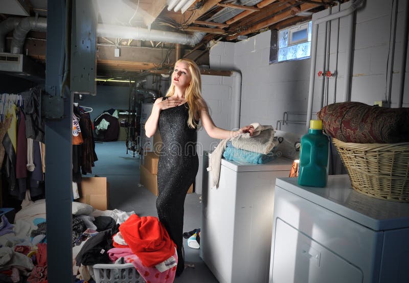 A young woman in in the basement doing laundry and chores while pretending to be in a stage play and acting with a spotlight on her. A young woman in in the basement doing laundry and chores while pretending to be in a stage play and acting with a spotlight on her.