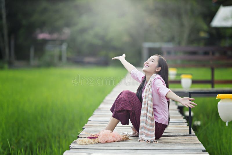 Lao beautiful young woman wearing local dress sitting on wooden bridge in green rice field happily. stock photos Lao beautiful young woman wearing local dress sitting on wooden bridge in green rice field happily. stock photos