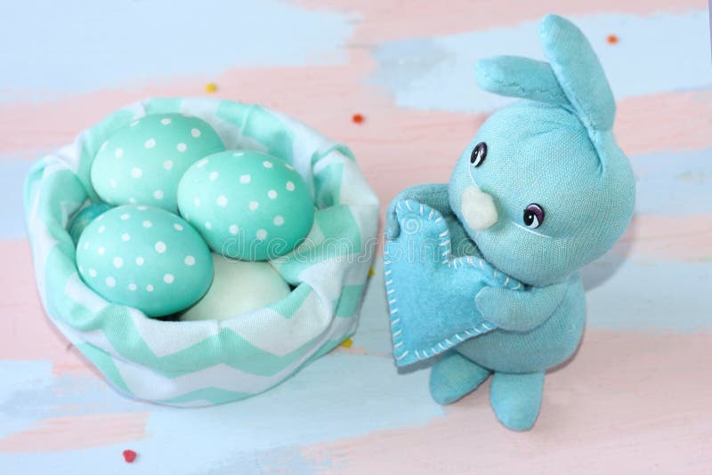 Lapin bleu-clair de Pâques cousu à la main près d'un panier de tissu avec les oeufs blanc bleu Travail manuel Carte de voeux pour photographie stock Lapin bleu-clair de Pâques cousu à la main près d'un panier de tissu avec les oeufs blanc bleu Travail manuel Carte de voeux pour photographie stock