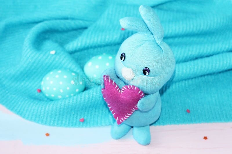 Lapin bleu de Pâques avec un coeur dans des ses pattes sur un fond bleu avec les oeufs tachetés bleus et blancs handmade Carte de image libre de droits Lapin bleu de Pâques avec un coeur dans des ses pattes sur un fond bleu avec les oeufs tachetés bleus et blancs handmade Carte de image libre de droits