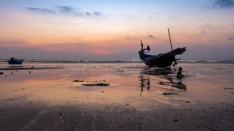 Lapso de tiempo del pequeño barco de pesca en la playa y reflejo del agua y del color naranja amarillo de la puesta de sol en la p