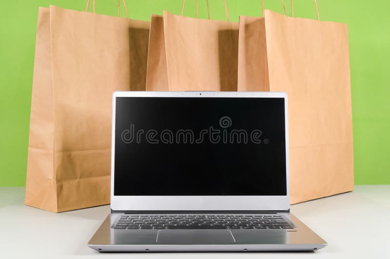 Laptop computer with blank screen against the background of paper bags with goods and purchases from online market