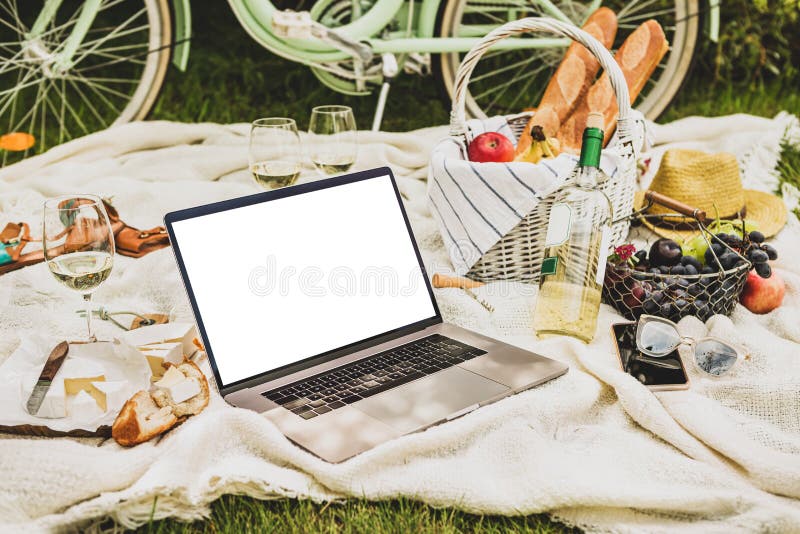 Laptop computer and french style outdoor picnic - wicker basket, wine and food