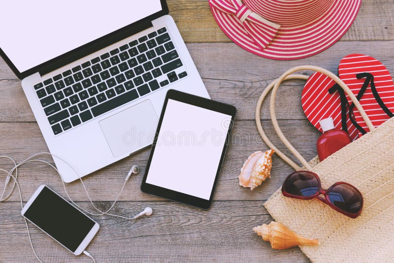 Laptop, digital tablet and smart phone with beach items over wooden background. View from above