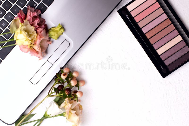Laptop with Flowers and Cosmetics on White Table. Freelancer Workspace