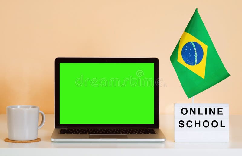 Laptop with a green screen on a table and a Brazil flag next to a display that says ONLINE SCHOOL. Laptop with a green screen on a table and a Brazil flag next to a display that says ONLINE SCHOOL