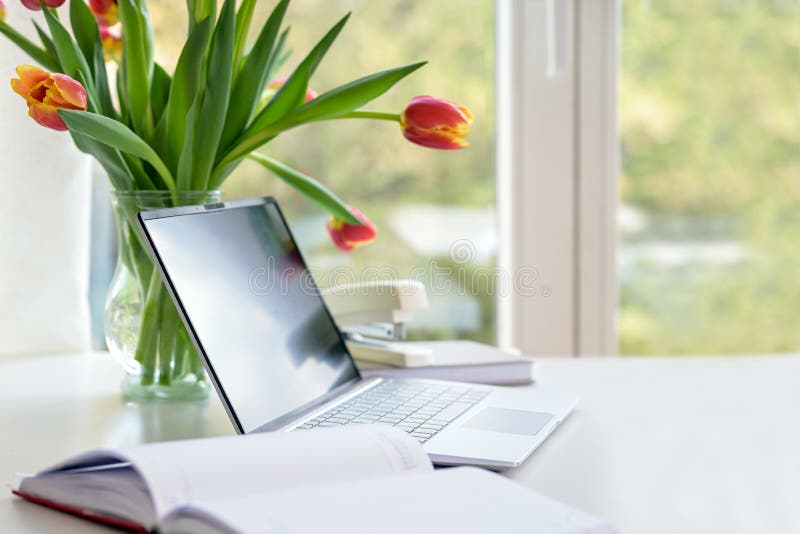 Laptop with organizer and a flower bouquet from tulips on a white desk by the window, business in the home office, copy space