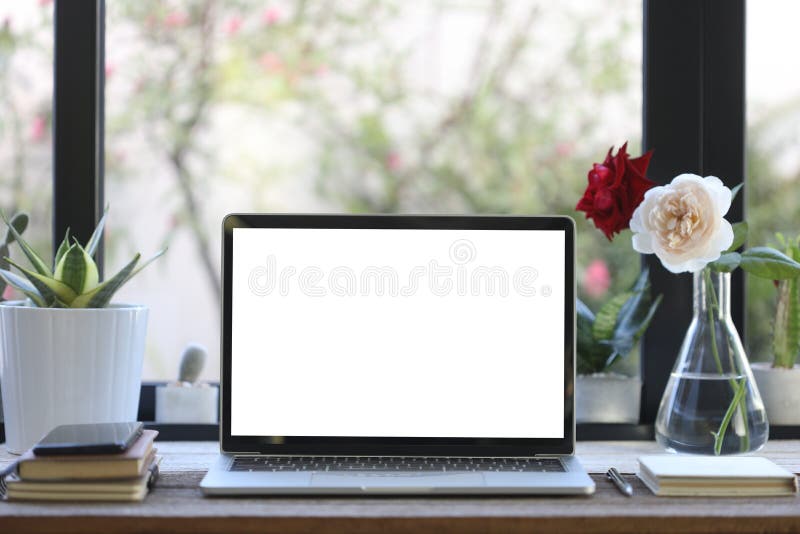 Laptop white blank screen with notebooks and rose vase on wooden table