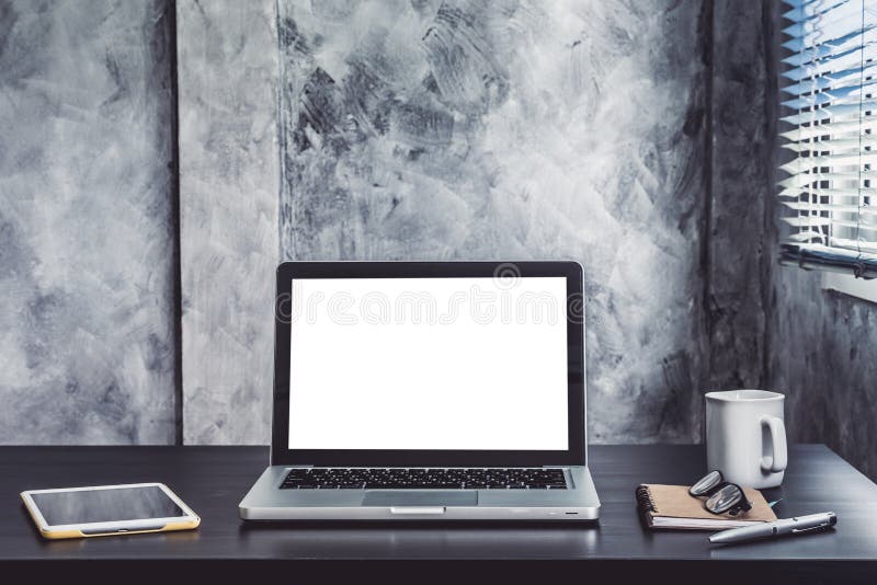 Laptop with white blank screen, white cup of coffee, tablet, notebook, pen and glasses on the desk.