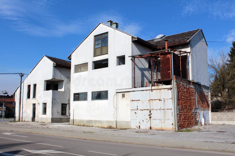 Large abandoned suburban family house with cracked dilapidated white facade and rusted sliding metal garage doors royalty free stock photo