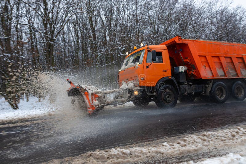 A large car with a plow clears the road from snow. Orange cargo special equipment is struggling with the elements in