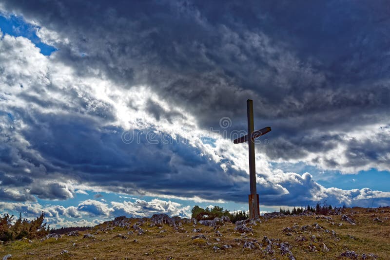 Wooden cross against a majestic sky filled with dramatic clouds. Low-angle image of an empty cross on a rugged hill. Good Friday, Resurrection, Easter. Jesus is risen. Hope. Dimensional landscape. Wooden cross against a majestic sky filled with dramatic clouds. Low-angle image of an empty cross on a rugged hill. Good Friday, Resurrection, Easter. Jesus is risen. Hope. Dimensional landscape.