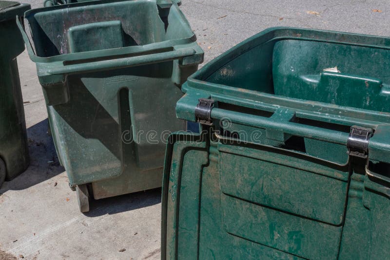 Large green trash cans, empty with lids open, curbside stock photography