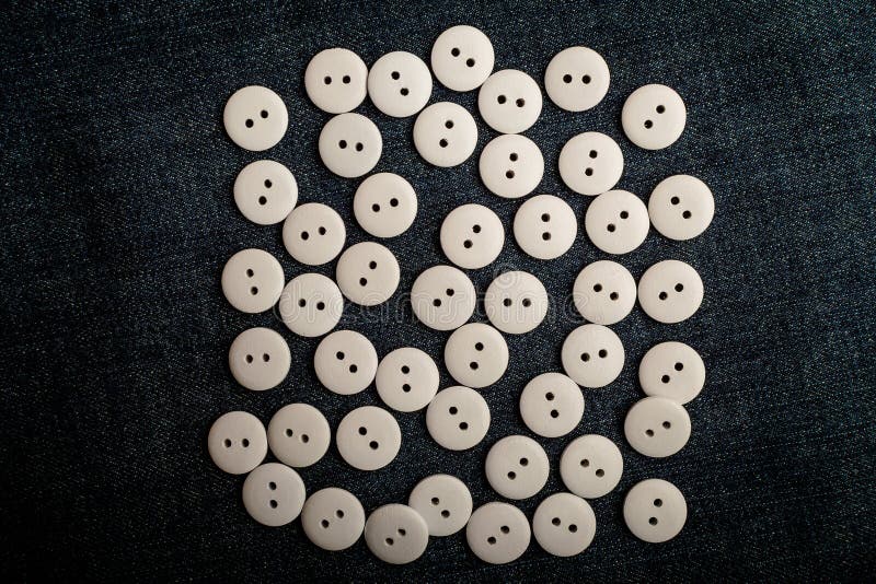 Large group pf delicate light white wooden buttons on dark grey textile material background, displayed centered, top view with space for text around, flat lay with laser cut wooden objects
