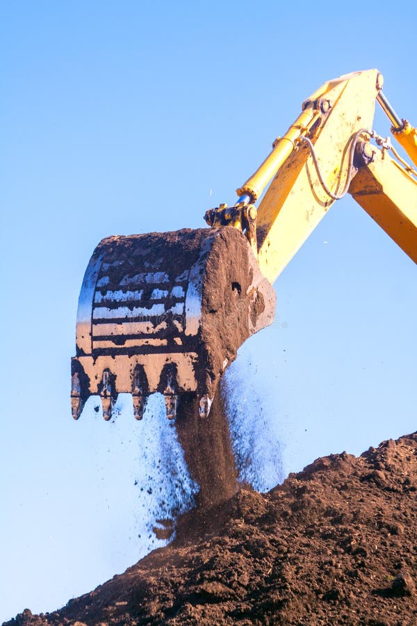 A large iron excavator bucket collects and pours sand rubble and stones in a quarry at the construction site of road facilities and houses