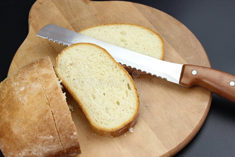 A Large Knife Cuts Thin Pieces of White Bread from a Rectangular Loaf