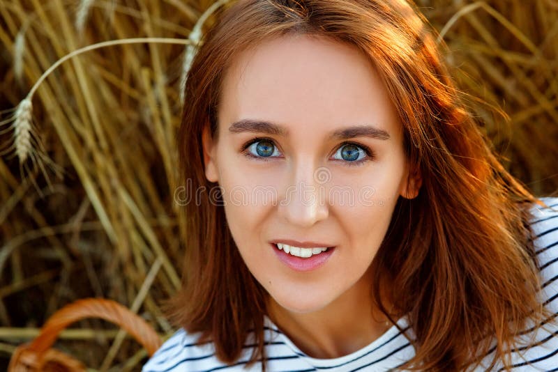 A large portrait of a young woman against the background of rye ears. Beautiful brunette on a wheat field at sunset .