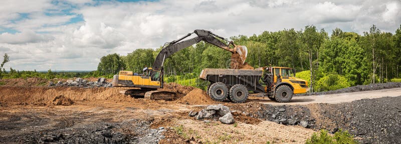 Large quarry dump truck. Big yellow mining truck at work site. Loading coal into body truck. Production useful minerals