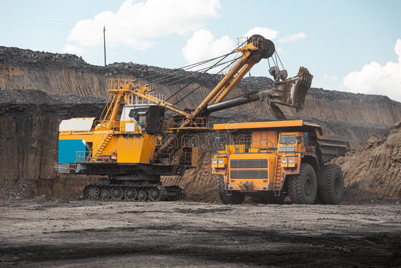 Large quarry dump truck. Big yellow mining truck at work site. Loading coal into body truck. Production useful minerals