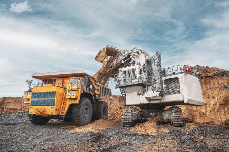 Large quarry dump truck. Big yellow mining truck at work site. Loading coal into body truck. Production useful minerals