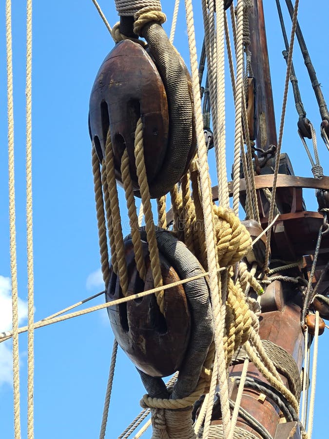 Large wooden blocks are attached to different ropes of a large sailing vessel.