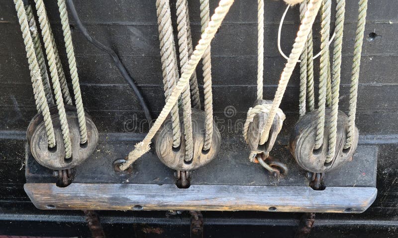 Large wooden blocks are attached to different ropes of a large sailing vessel.