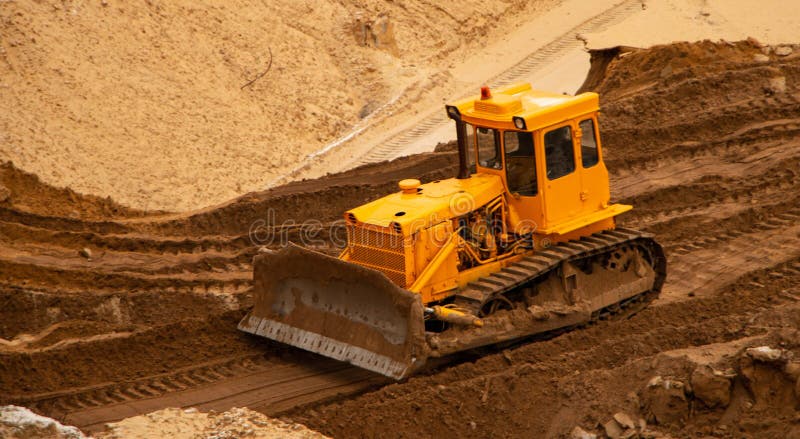 Large yellow caterpillar industrial tractor, iron dump shifts sand and ground, lines road for transport inside development of