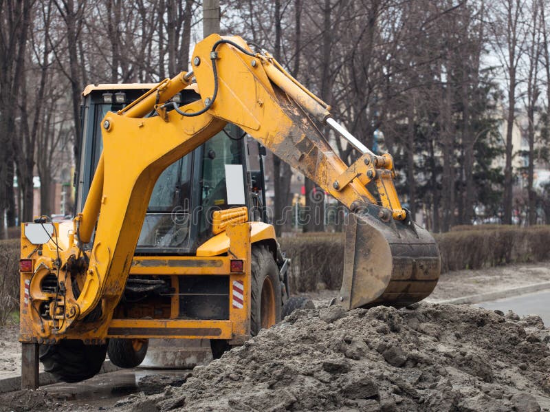 A large yellow excavator stands in the middle of the street near the dug hole stock image A large yellow excavator stands in the middle of the street near the dug hole stock image