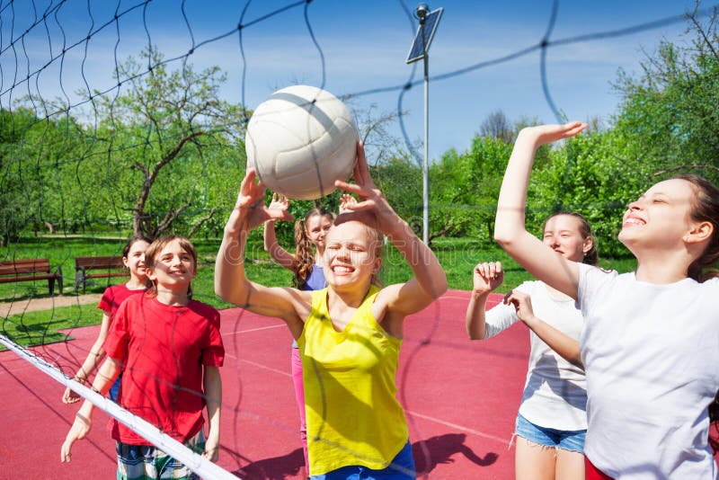 Excited teens play near the volleyball net on the court during sunny summer day outside. Excited teens play near the volleyball net on the court during sunny summer day outside