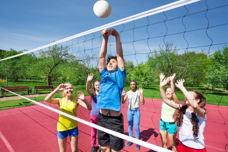 Teens all are with arms up play volleyball near net on the playing court during sunny summer day. Teens all are with arms up play volleyball near net on the playing court during sunny summer day