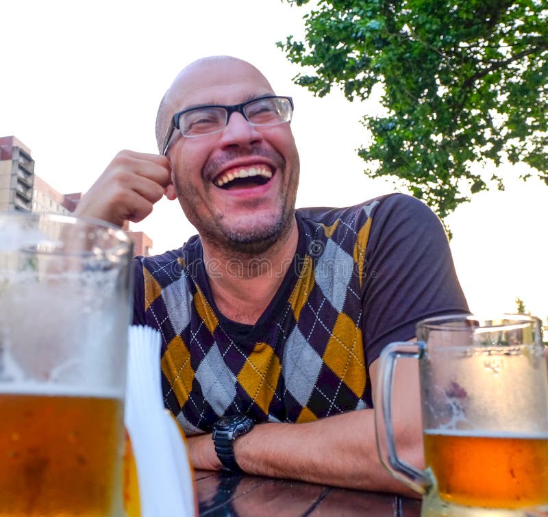 Las bromas de consumición de la sidra del hombre, sonrisas Un hombre joven bebe la sidra en un café abierto y miradas en la dista foto de archivo Las bromas de consumición de la sidra del hombre, sonrisas Un hombre joven bebe la sidra en un café abierto y miradas en la dista foto de archivo