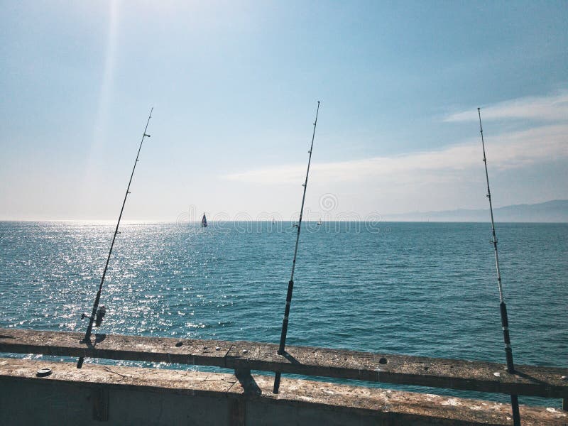 Las cañas de pescar están esperando morder en el embarcadero Contra la perspectiva de los yates de la navegación Un día de verano caliente en California , los E