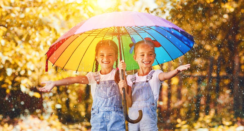 Las hermanas divertidas felices hermanan a la muchacha del niño con el paraguas en otoño
