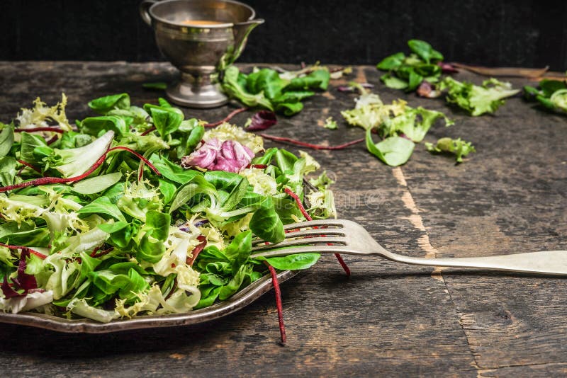 Las hojas del verde mezclan la ensalada con la bifurcación y el vestido en la tabla de cocina rústica, cierre para arriba imagen de archivo Las hojas del verde mezclan la ensalada con la bifurcación y el vestido en la tabla de cocina rústica, cierre para arriba imagen de archivo