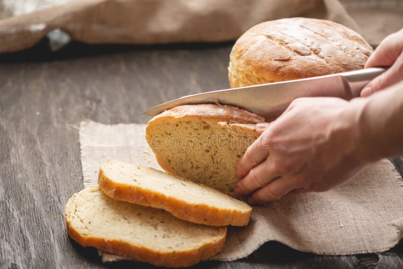 Las manos cortaron con un pan fresco natural hecho en casa del cuchillo con una corteza de oro en fondo de madera Productos de la fotos de archivo