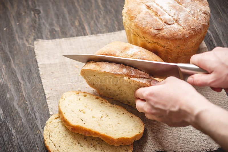 Las manos cortaron con un pan fresco natural hecho en casa del cuchillo con una corteza de oro en fondo de madera Productos de la fotos de archivo