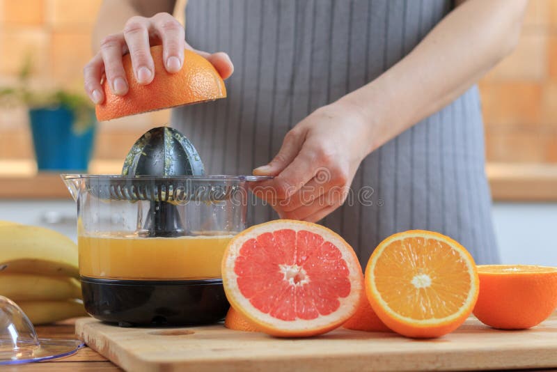 Las manos de la mujer están llevando a cabo una mitad del pomelo y están haciendo el jugo imagen de archivo Las manos de la mujer están llevando a cabo una mitad del pomelo y están haciendo el jugo imagen de archivo
